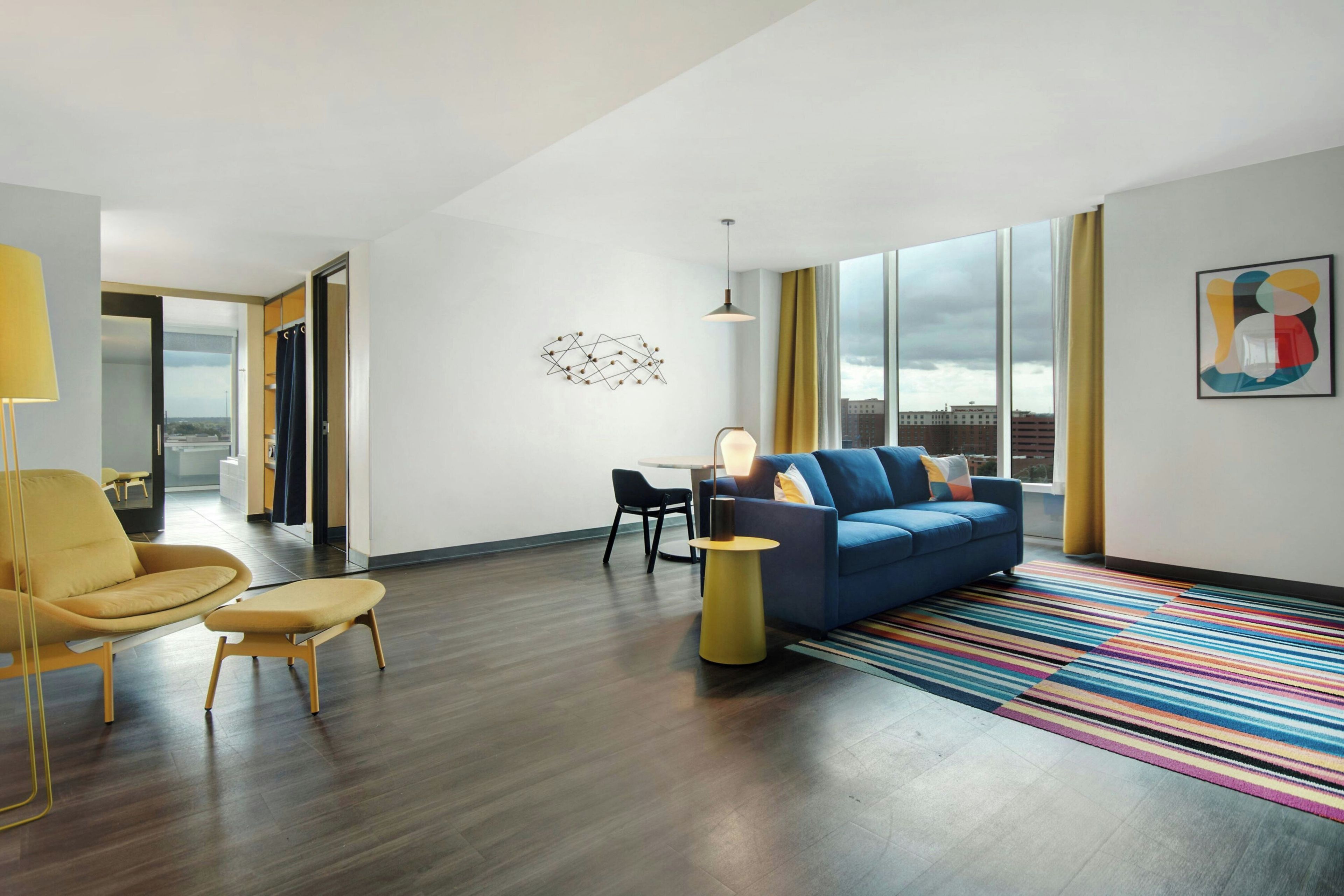 A modern living room with a blue sofa, yellow armchair, and a colorful striped rug.