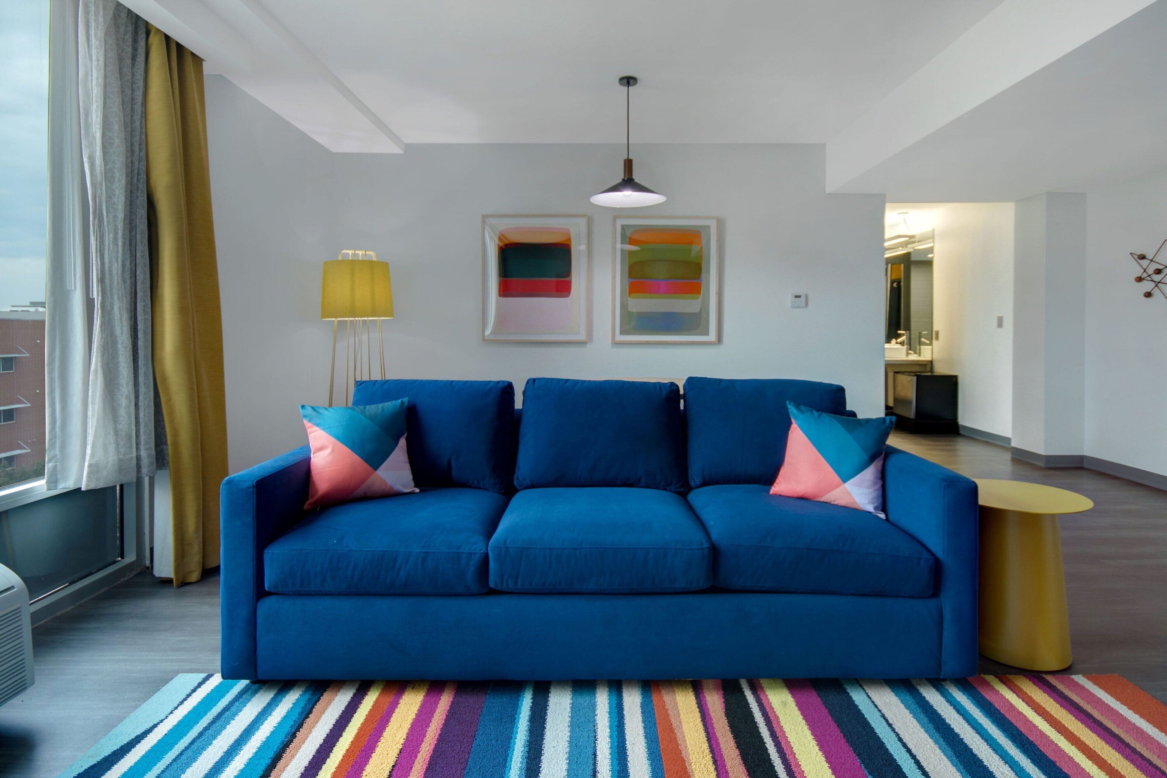 A modern living room with a blue sofa, colorful striped rug, and abstract art on the wall.