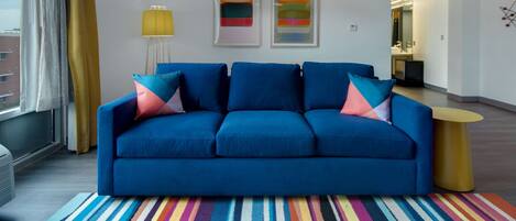 A modern living room with a blue sofa, colorful striped rug, and abstract art on the wall.