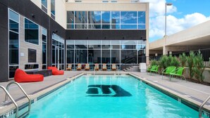 A swimming pool with lounge chairs and a modern building with large windows in the background. - Aloft by Marriott Oklahoma City Downtown - Bricktown (Oklahoma City)