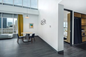A modern hotel room with a large window, a dining area with a table and chairs, and a built-in wardrobe. - Aloft by Marriott Oklahoma City Downtown - Bricktown (Oklahoma City)