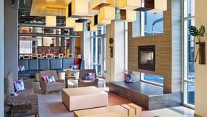 A modern lobby with a fireplace, seating areas, and a large window providing a view of the outdoors. - Aloft by Marriott Oklahoma City Downtown - Bricktown (Oklahoma City)