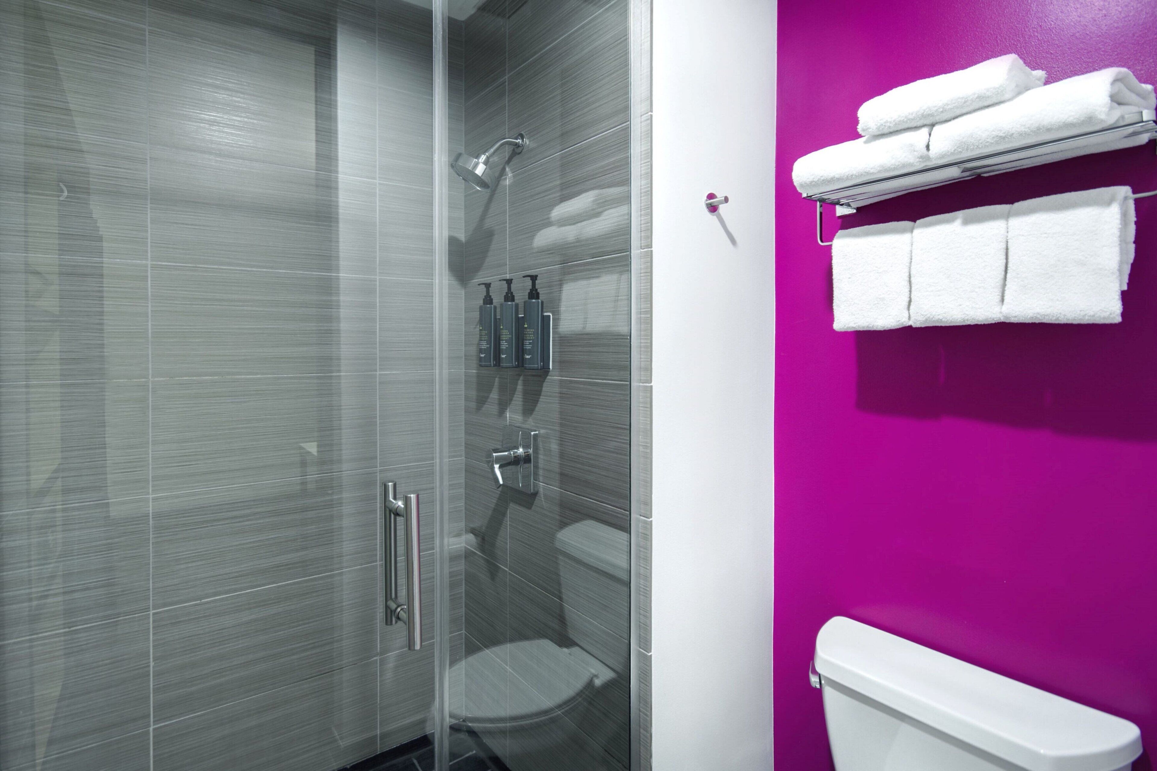 A modern bathroom with a glass shower enclosure, a toilet, and a wall-mounted towel rack with folded towels.