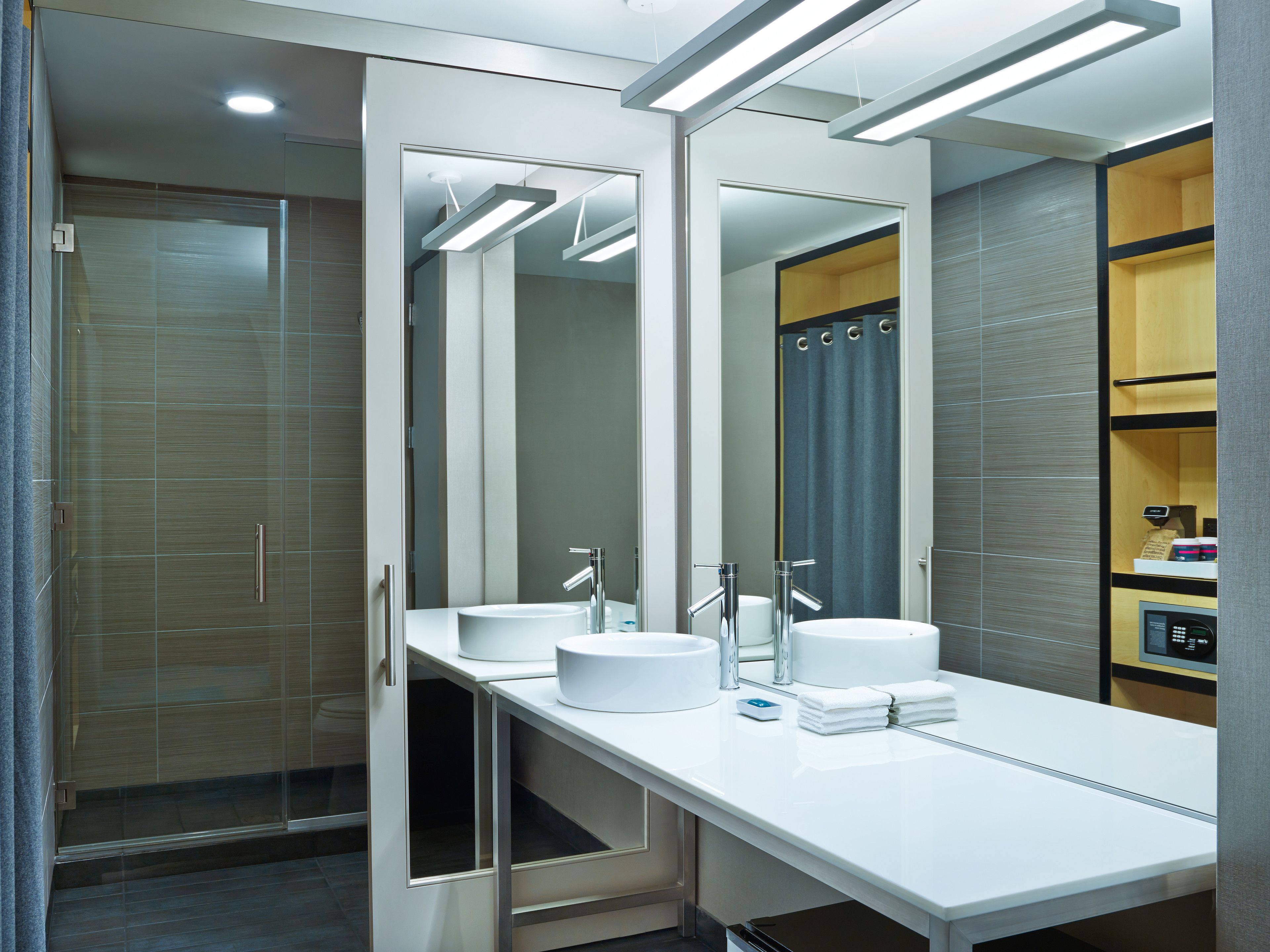 A modern bathroom with a large mirror, two sinks, and a shower area.
