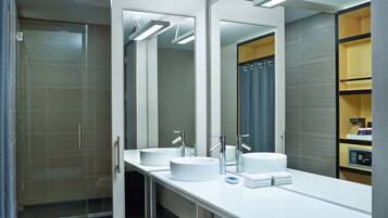A modern bathroom with a large mirror, two sinks, and a shower area.