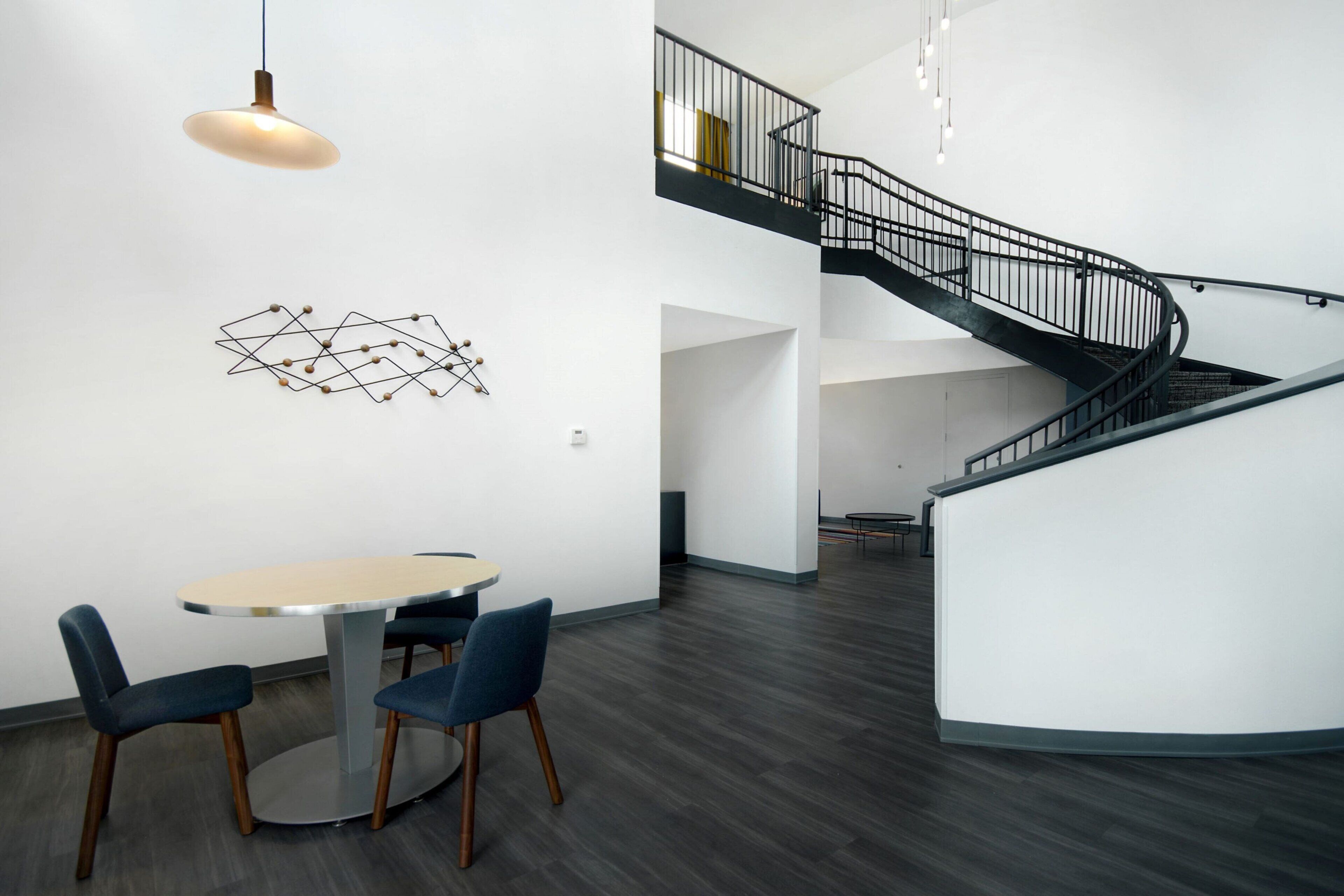 A modern interior with a round table and chairs, a spiral staircase, and a geometric wall art piece.