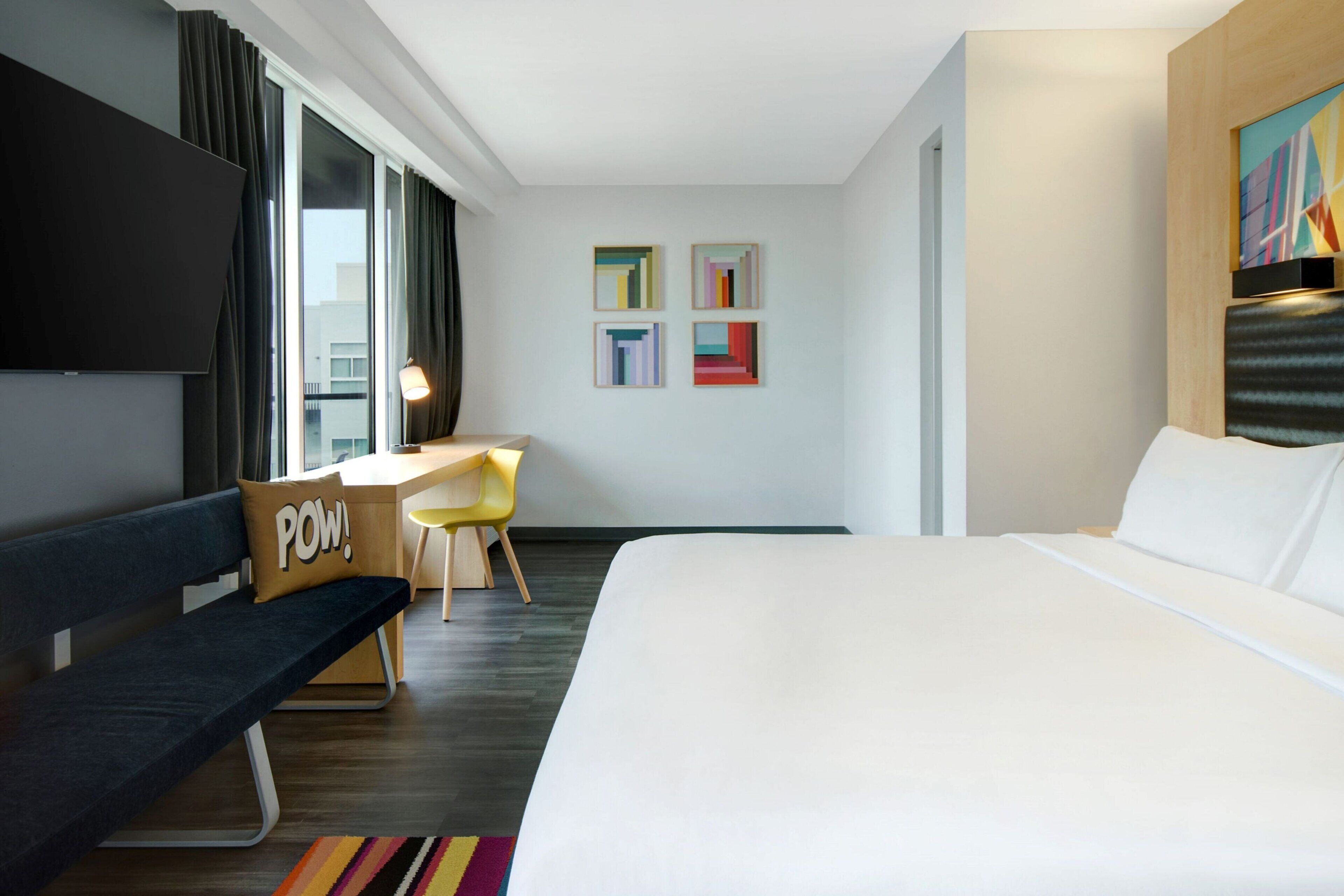 A modern hotel room with a large bed, a desk, a chair, and a TV.