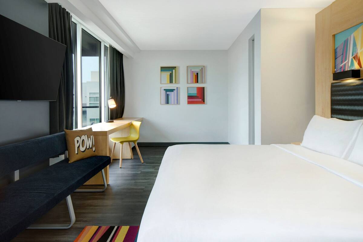 A modern hotel room with a large bed, a desk, a chair, and a TV.