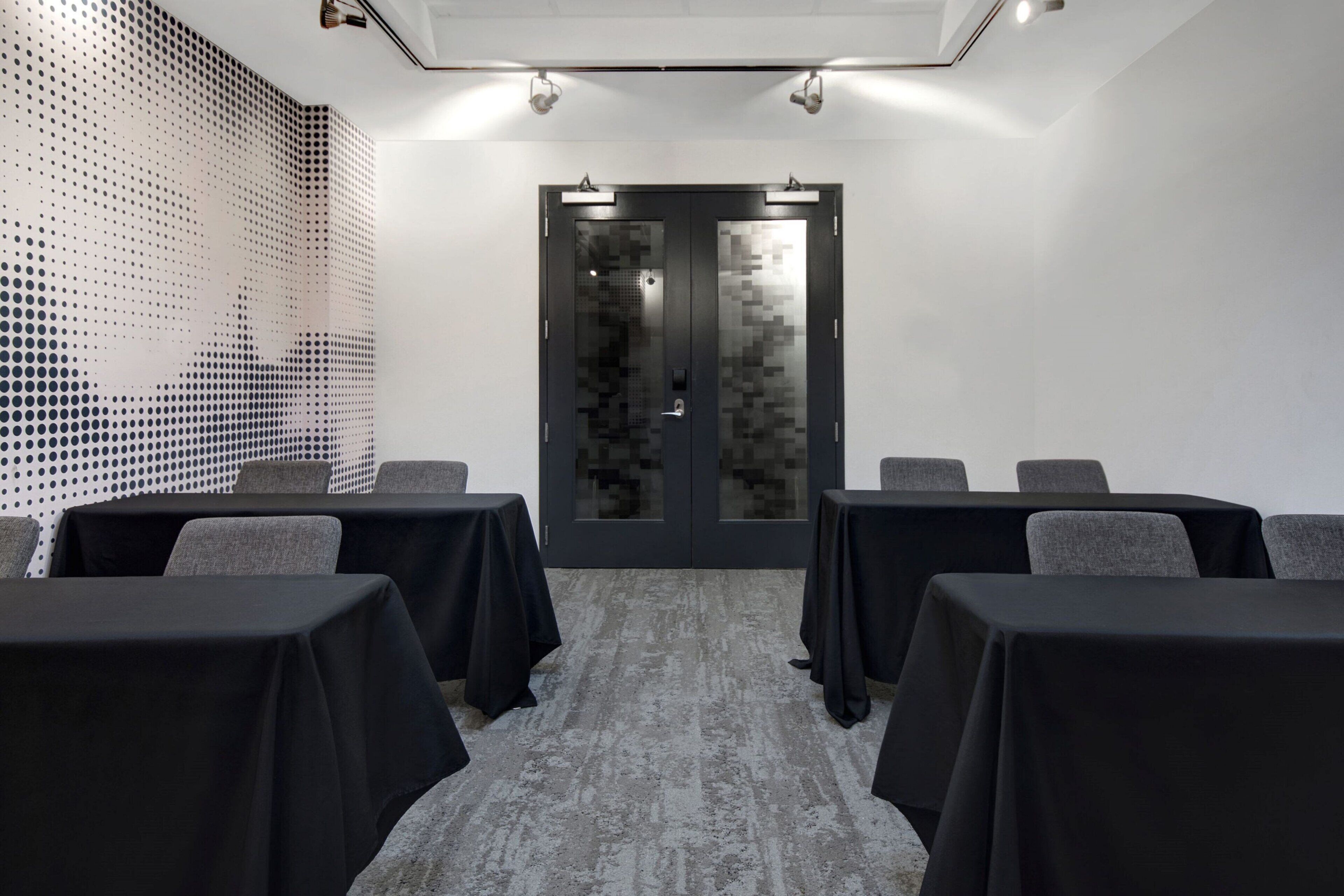 A conference room with a modern design, featuring a patterned wall, a glass door, and tables with black tablecloths.