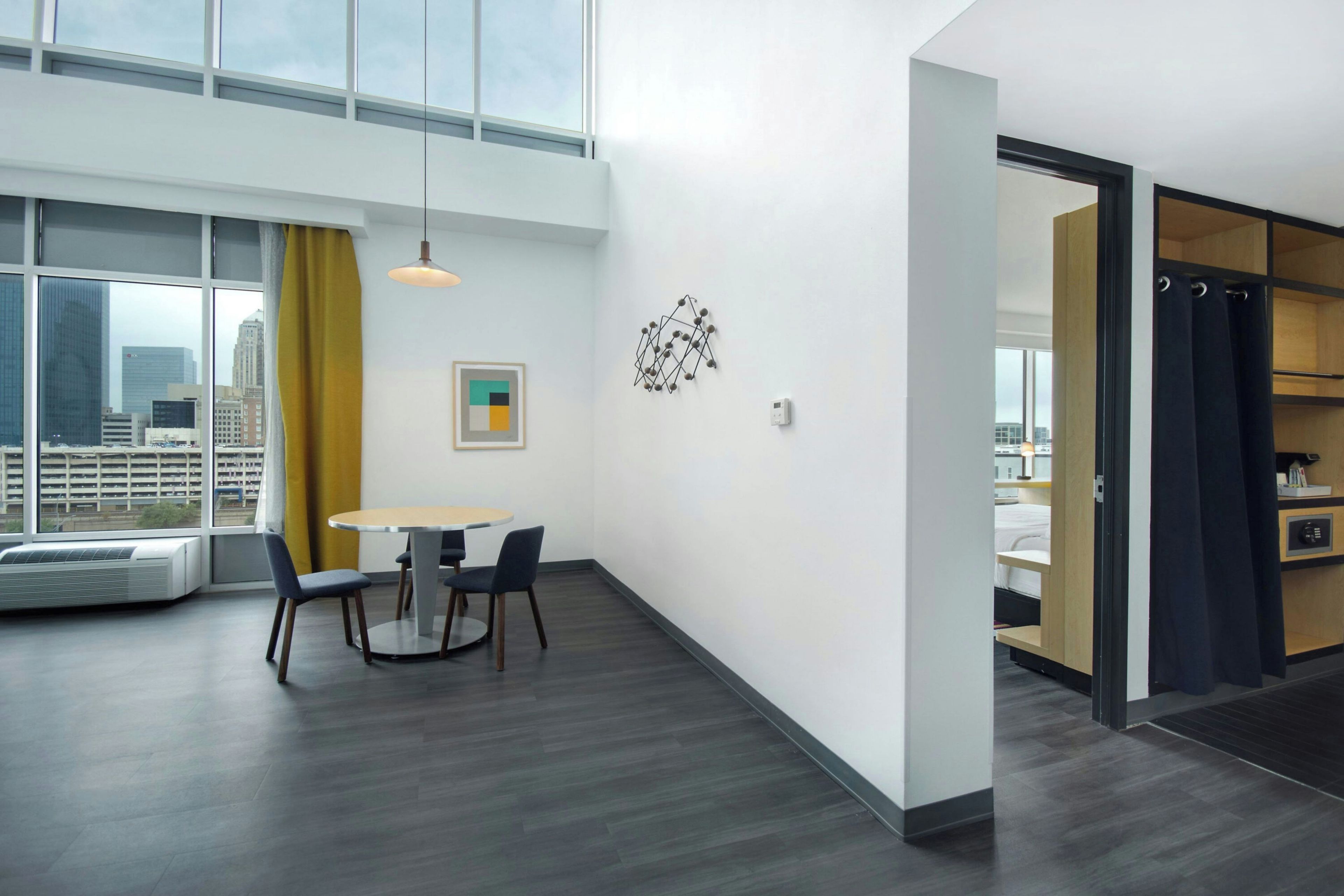A modern hotel room with a dining area, large windows, and a view of the cityscape.