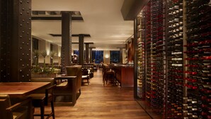 A restaurant with wooden flooring, metal pillars, and a wine rack filled with bottles. - JW Marriott Houston Downtown (Houston)