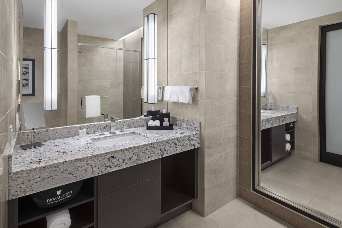 A modern bathroom with a granite countertop sink, a large mirror, and a walk-in shower.