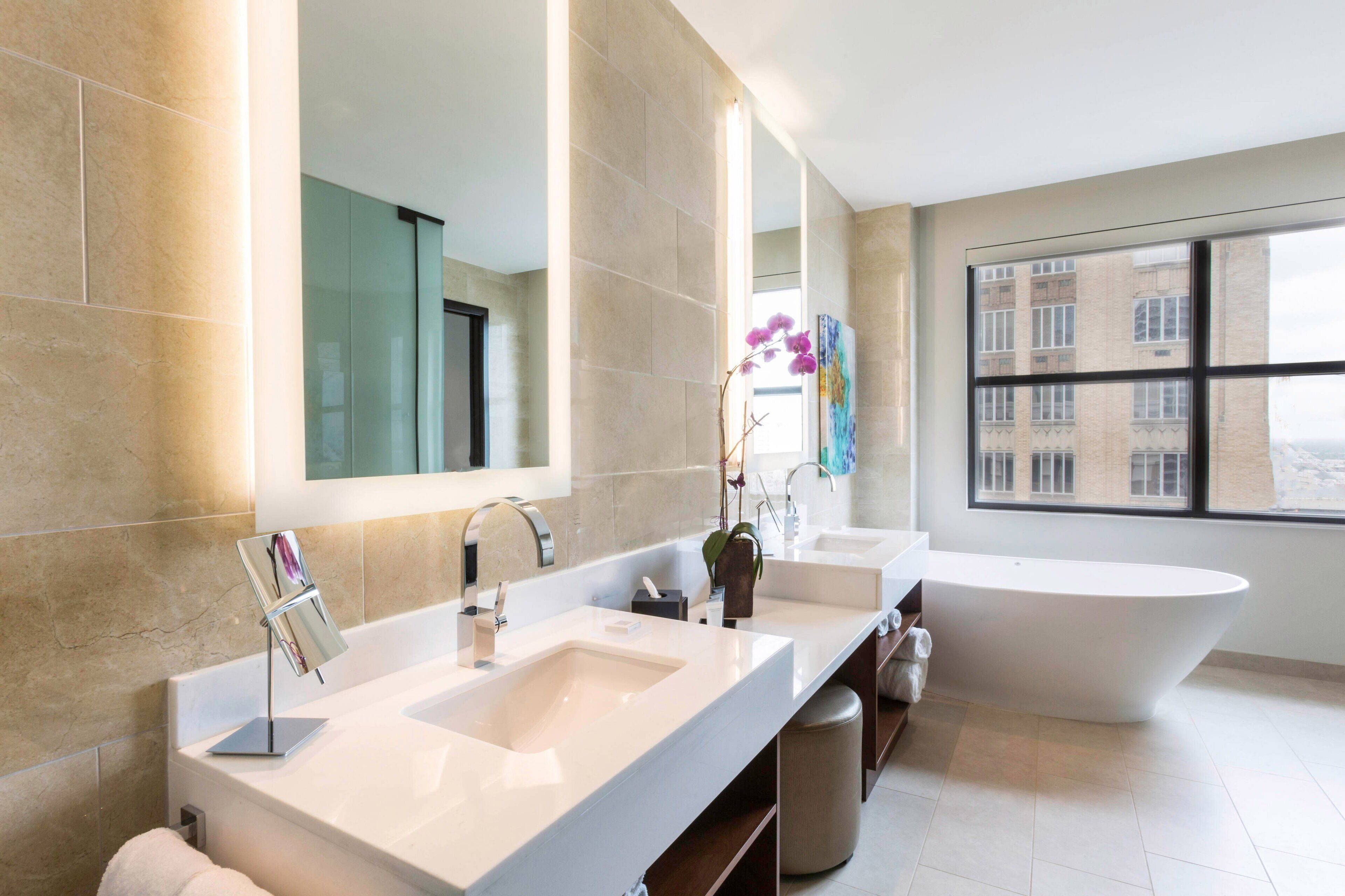 Un baño moderno con dos lavamanos, un espejo grande y una bañera independiente.
