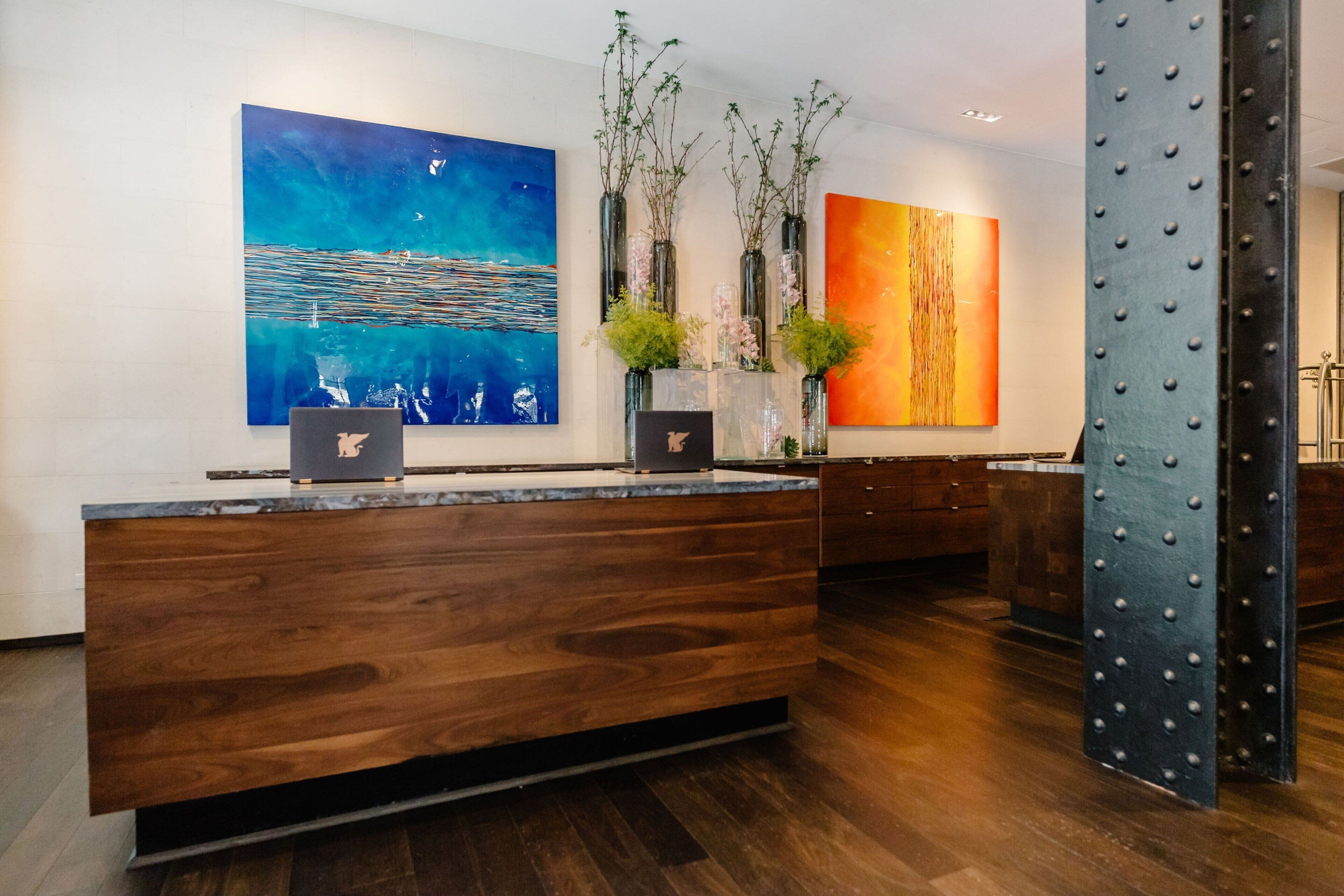 A modern reception area with a wooden reception desk, a large abstract painting, and a metal column.