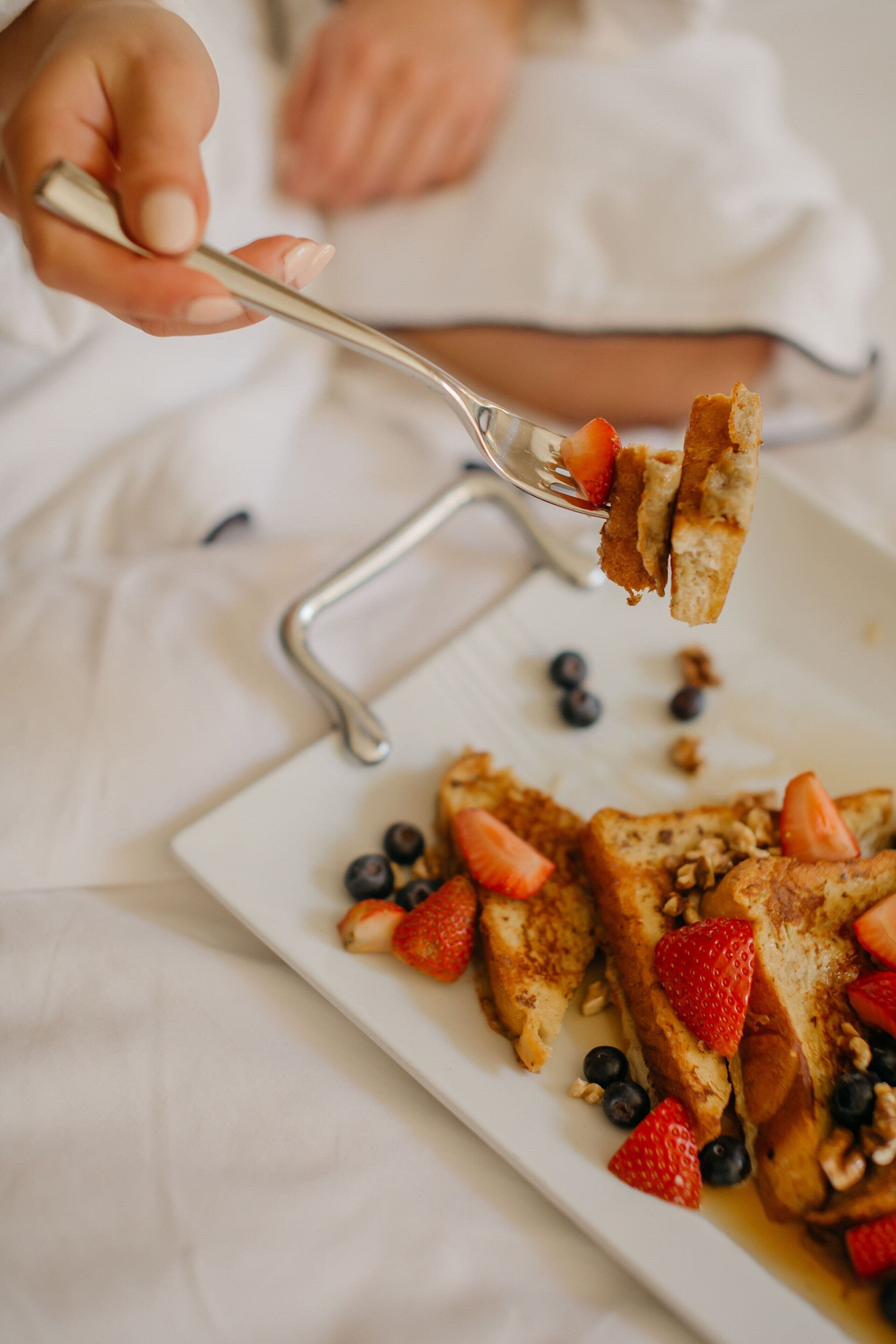 A person holding a fork with a piece of toast and strawberries.