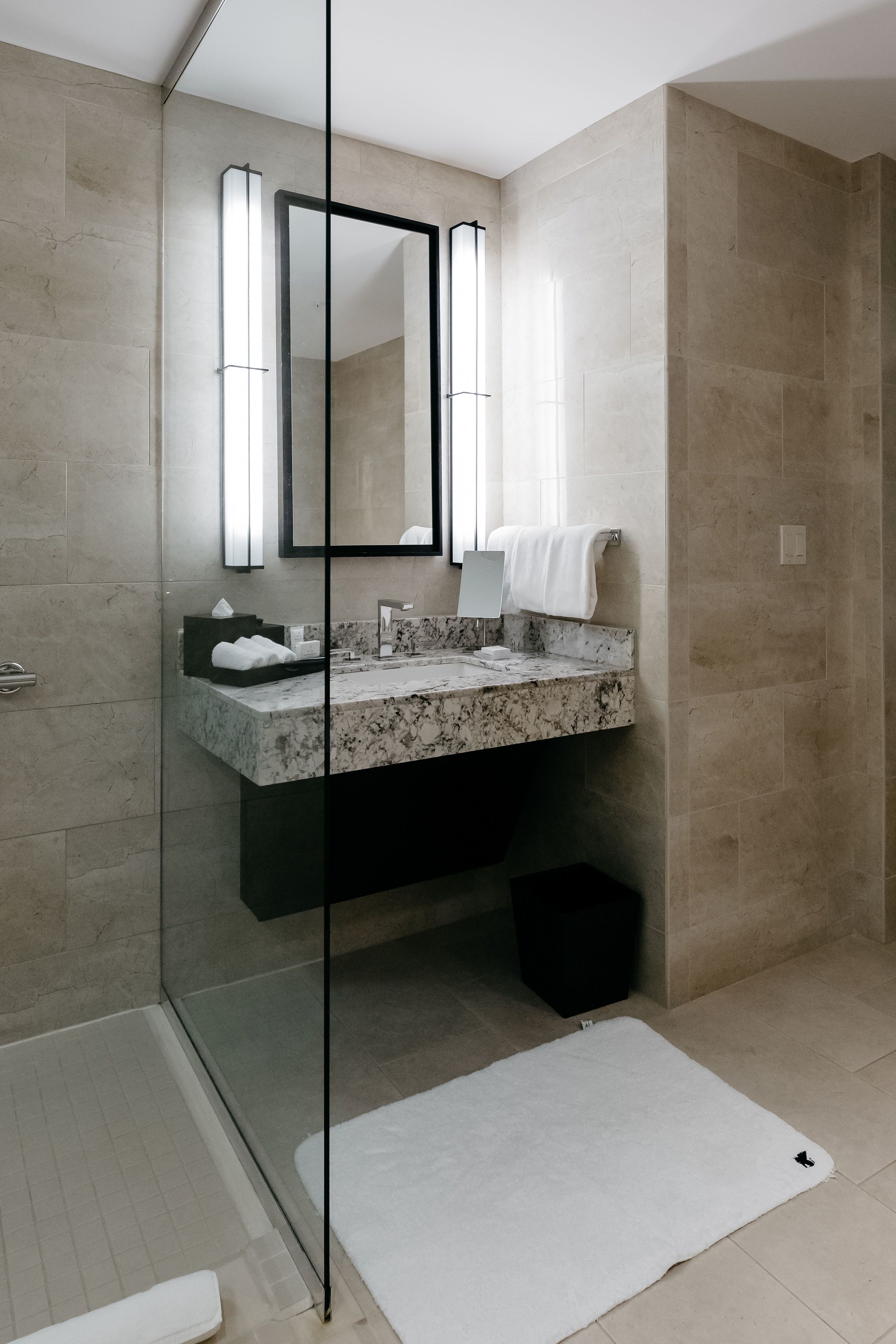 A modern bathroom with a glass shower enclosure, a marble sink, and a large mirror.