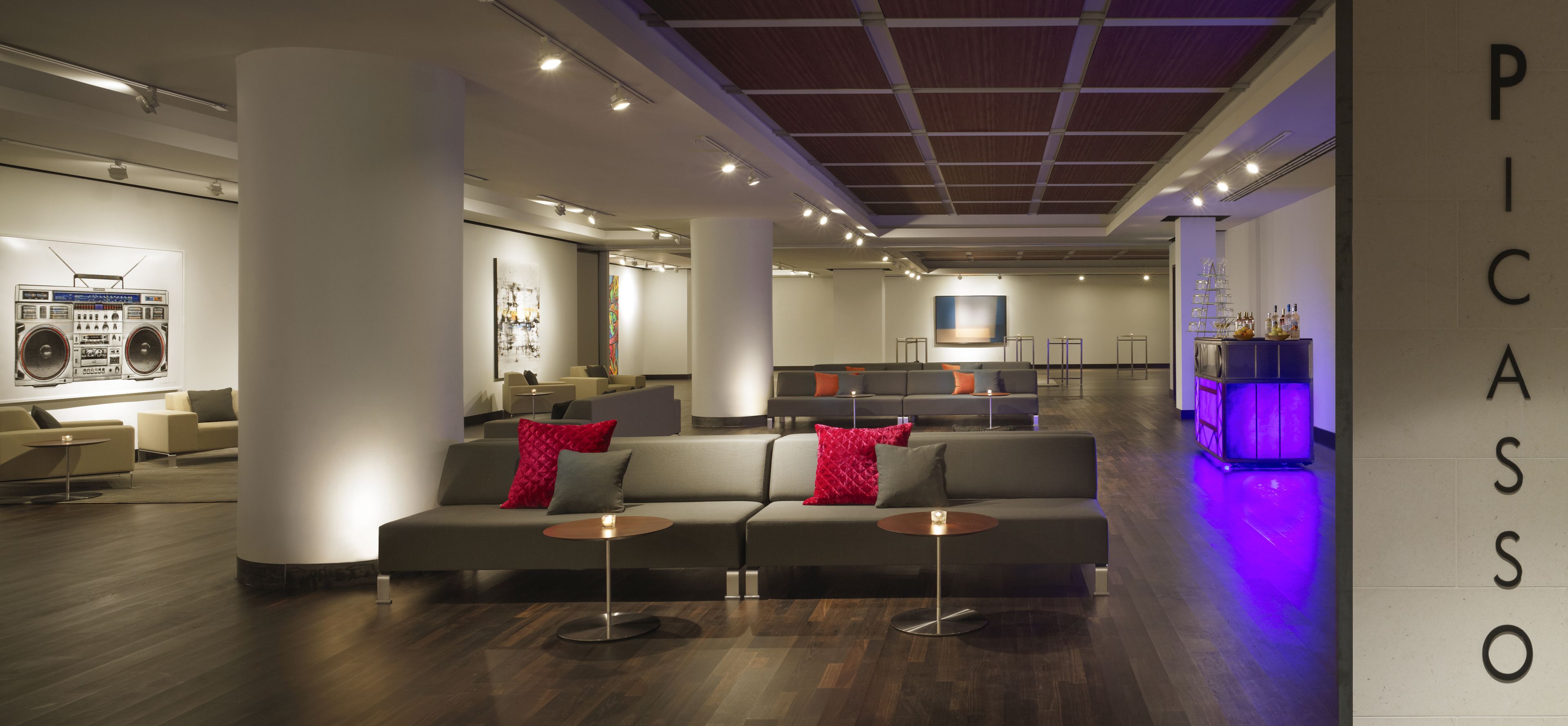 A modern lobby with a sofa, a bar area, and a large wall with the text "PICASSO".