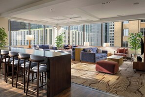 A spacious living area with a bar, seating, and large windows offering views of buildings. - JW Marriott Houston Downtown (Houston)