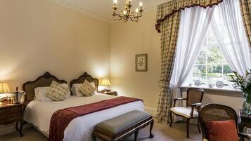 Een slaapkamer met een groot bed, twee nachtkastjes met lampen, een stoel, een raam met gordijnen en een kroonluchter.