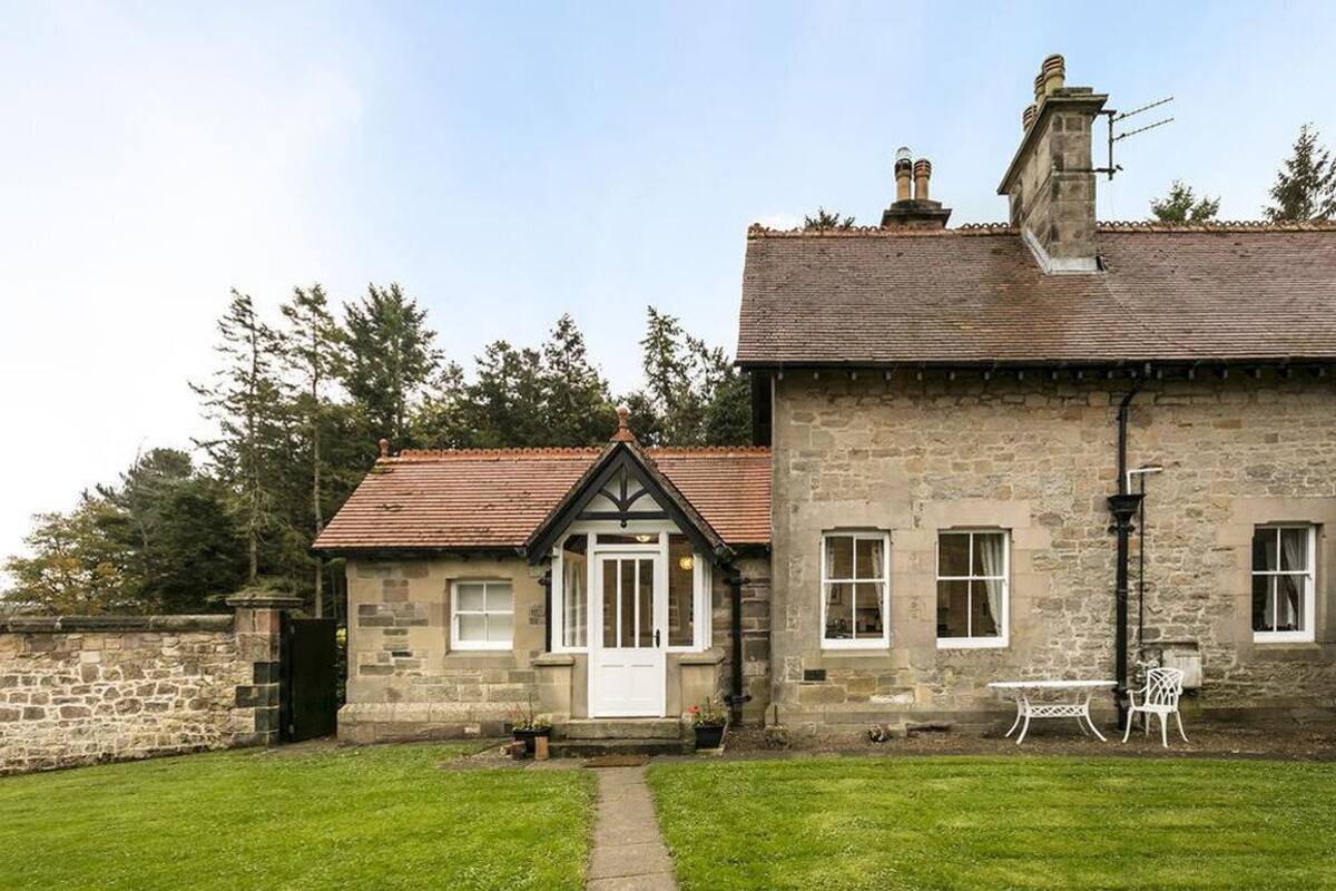 A stone house with a tiled roof, a small porch, and a lawn with a table and chairs.