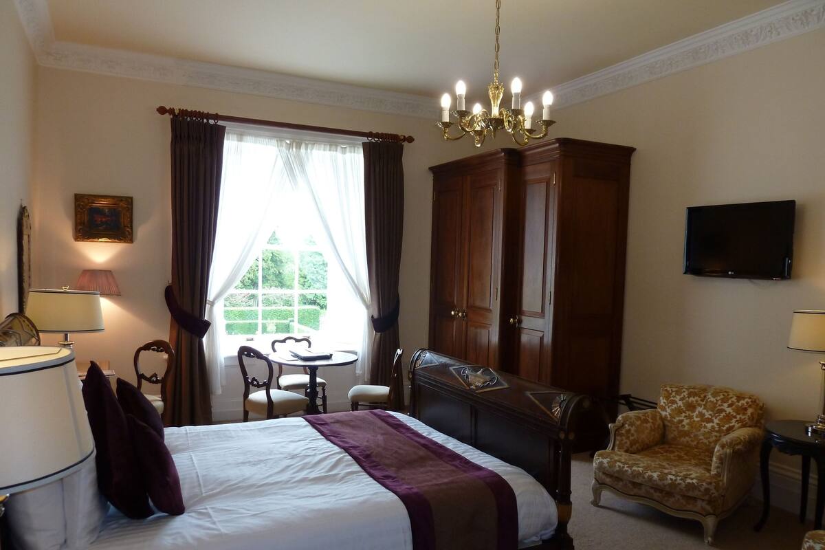 A hotel room with a bed, a desk, a chair, a television, and a wardrobe.