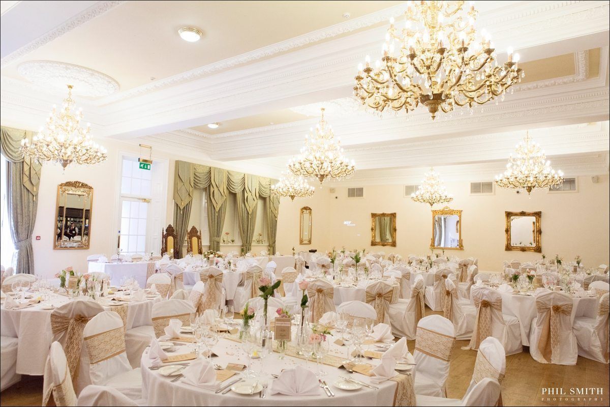 A banquet hall with multiple round tables, each set with white tablecloths, chairs, and centerpieces.