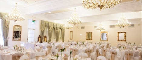 A banquet hall with multiple round tables, each set with white tablecloths, chairs, and centerpieces.
