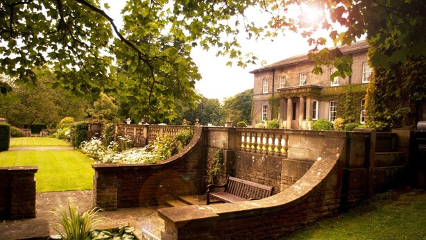 A garden with a curved stone wall, a bench, and a well-maintained lawn. - Doxford Hall Hotel & Spa (Chathill)