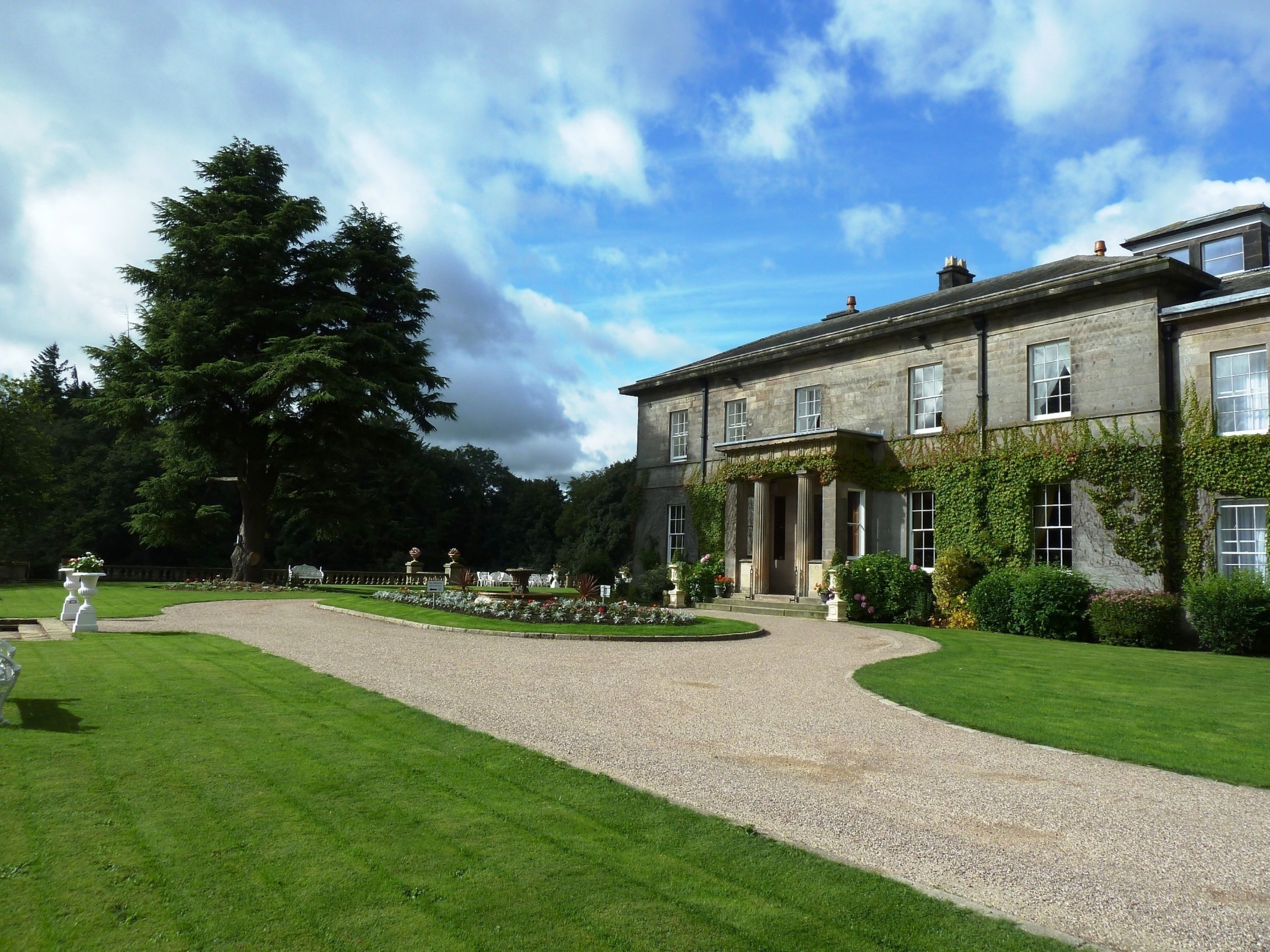 A large, historic stone building with a formal entrance and a gravel driveway leading to it.
