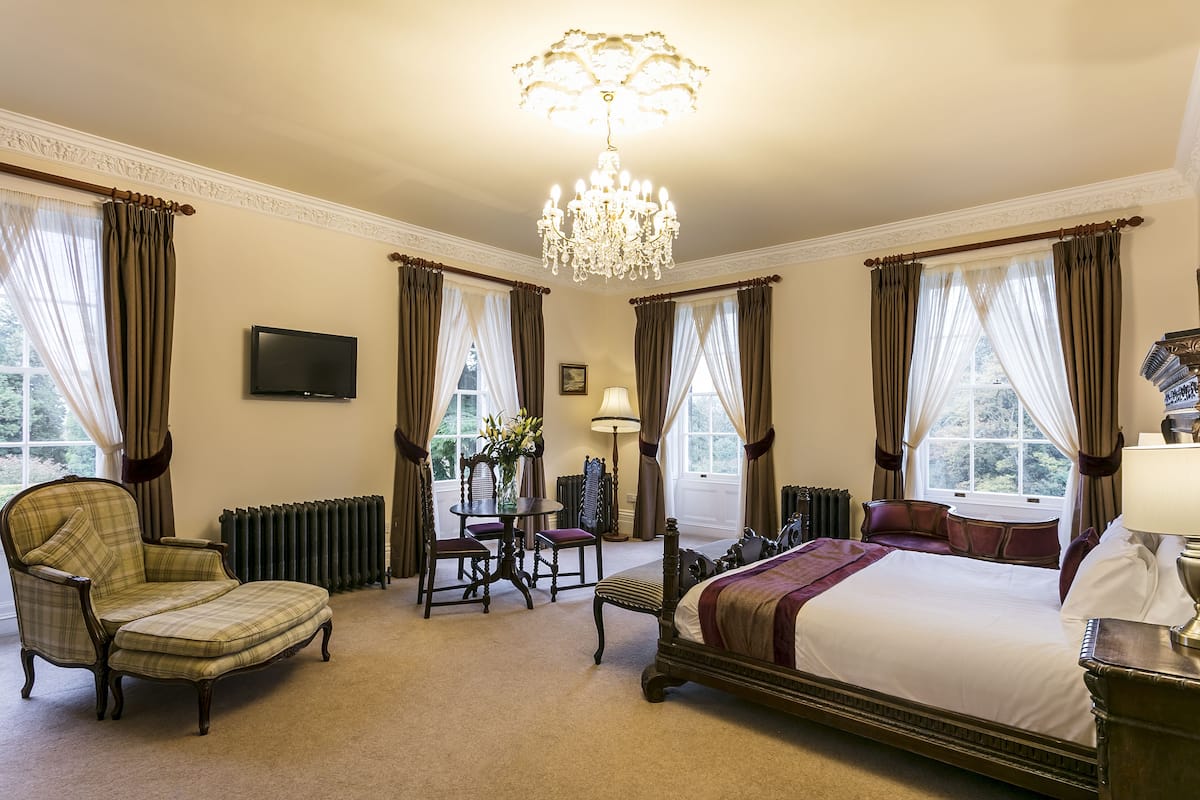 A spacious bedroom with a large bed, a sitting area with a chair and table, and a chandelier.