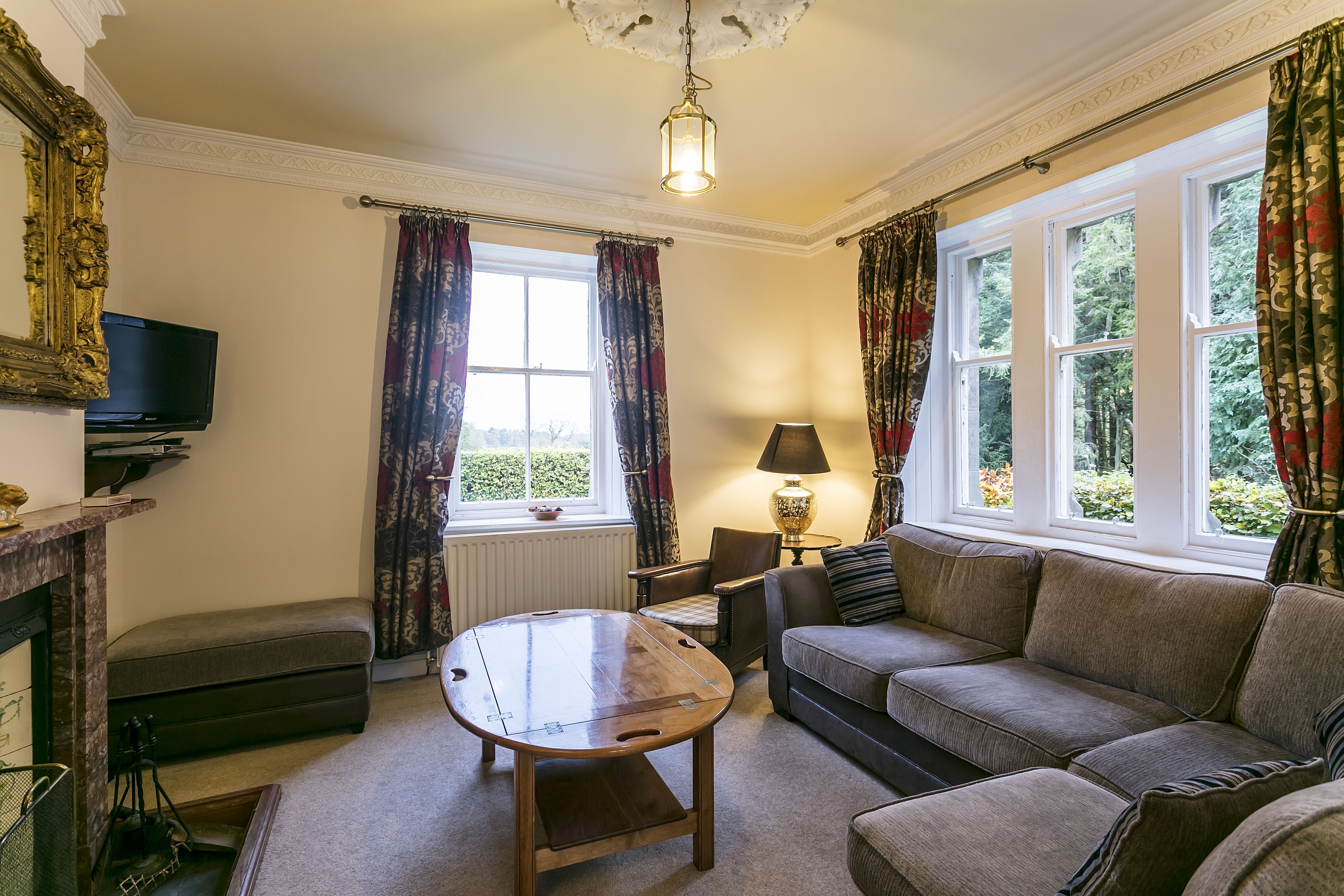 A living room with a sofa, a coffee table, a fireplace, a television, and large windows with curtains.