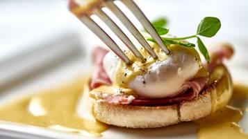 A close-up of a breakfast dish with poached eggs, ham, and hollandaise sauce on toast, garnished with a leaf.