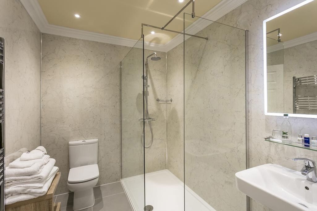 A modern bathroom with a glass-enclosed shower, a toilet, and a sink with a mirror above.