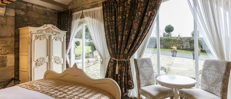 A bedroom with a bed, a dresser, and a view of a garden through large windows.