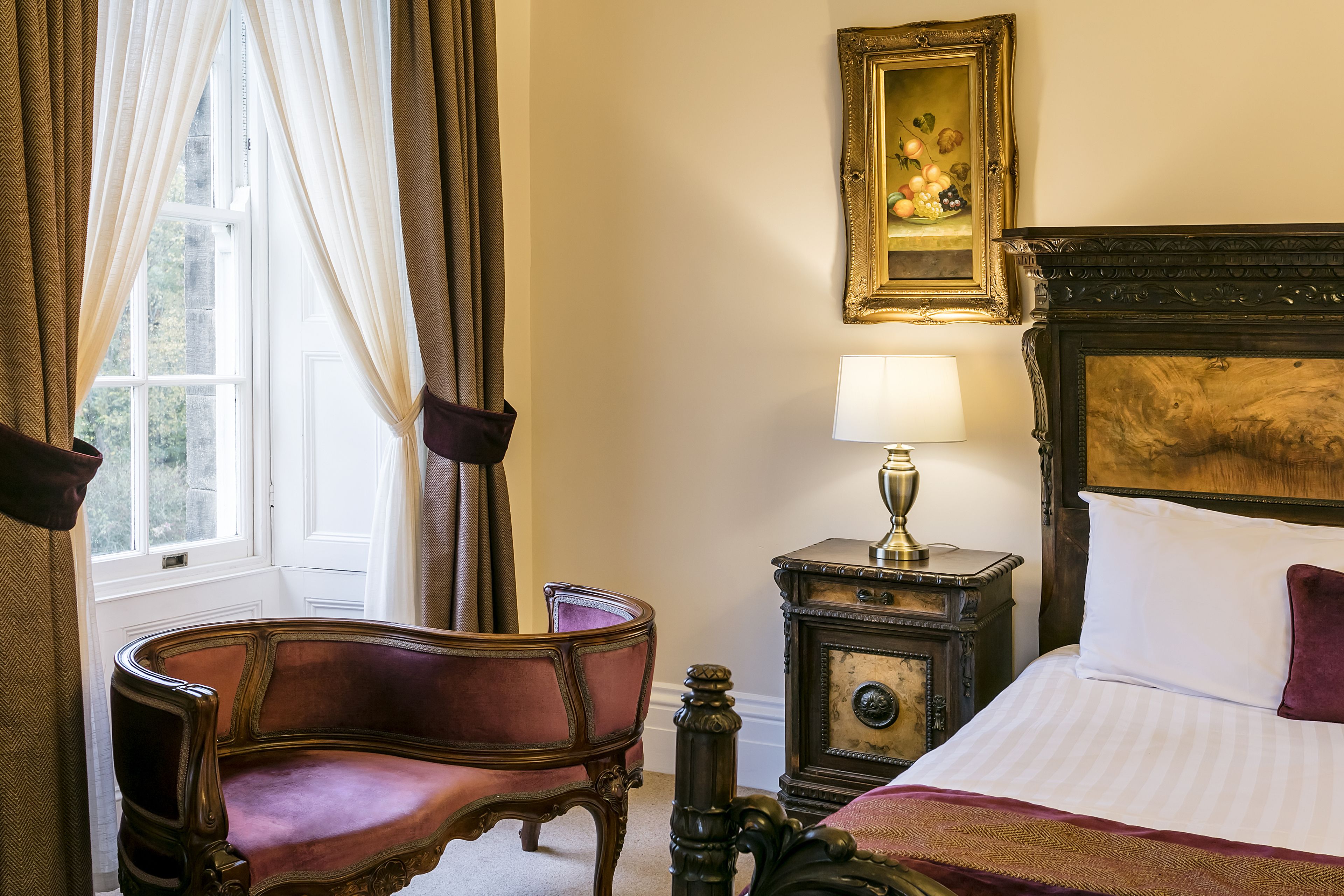 Una habitación con cama, una silla, una mesita de noche, una lámpara y una ventana con cortinas.