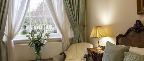 A bedroom with a bed, a chair, a nightstand, a lamp, and a window with curtains.