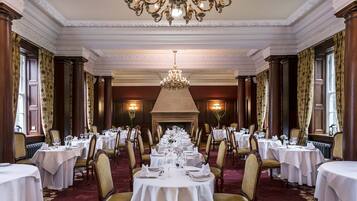 Un comedor formal con varias mesas redondas dispuestas para una comida, elegantes candelabros y decoración clásica.