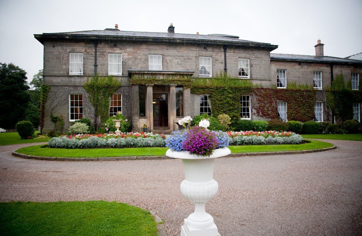 A large stone building with a formal entrance, a well-maintained garden with flower beds, and a gravel driveway.