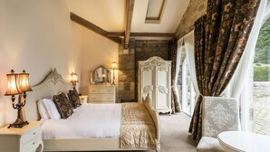 A bedroom with a bed, bedside lamps, a dresser, a mirror, a wardrobe, and a chair by a window with curtains. - Doxford Hall Hotel & Spa (Chathill)
