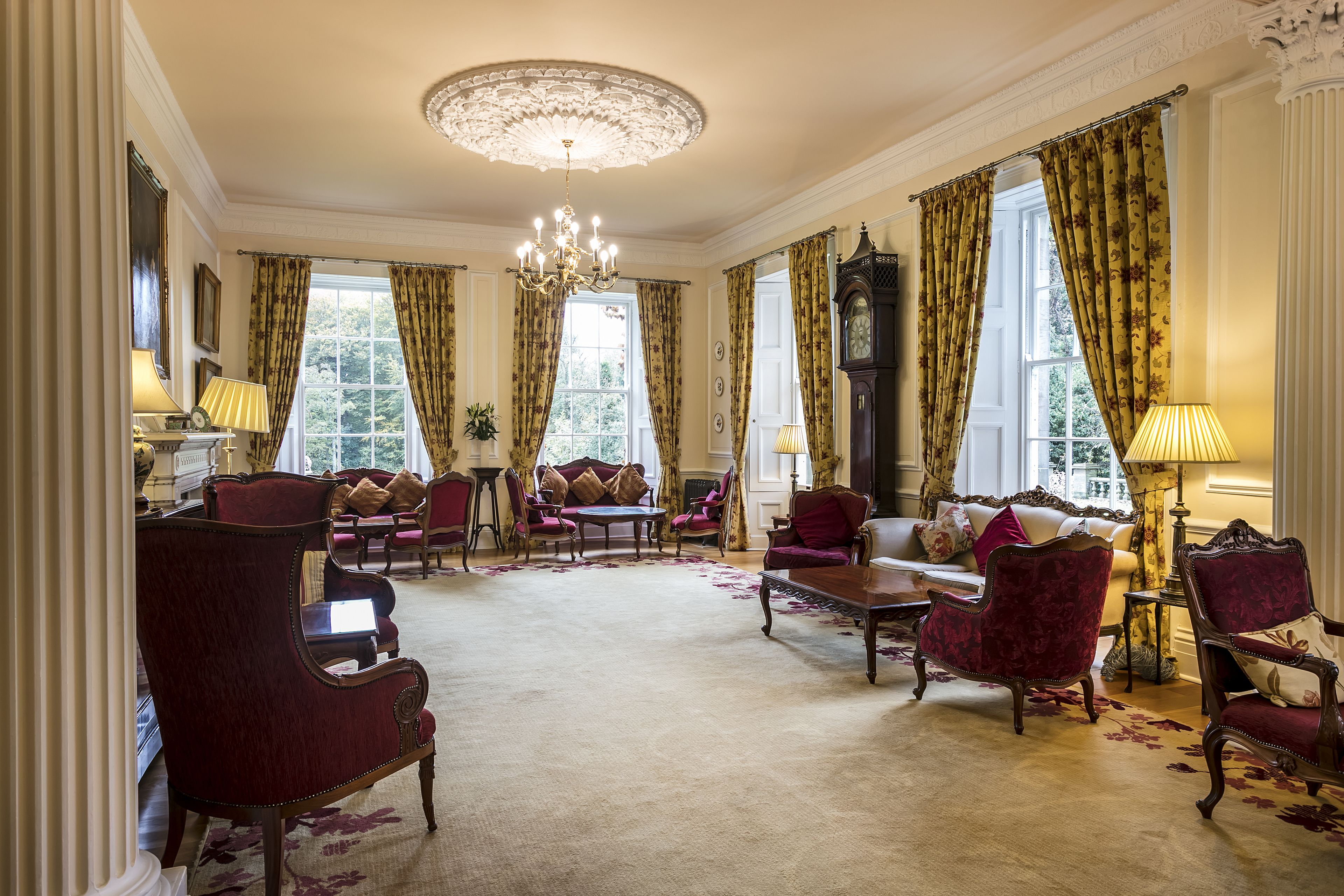 A spacious room with a large chandelier, elegant furniture, and large windows with curtains.