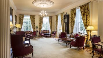 A spacious room with a large chandelier, elegant furniture, and large windows with curtains.