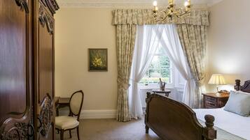 A bedroom with a wooden bed, a chair, a nightstand with a lamp, and a window with curtains.