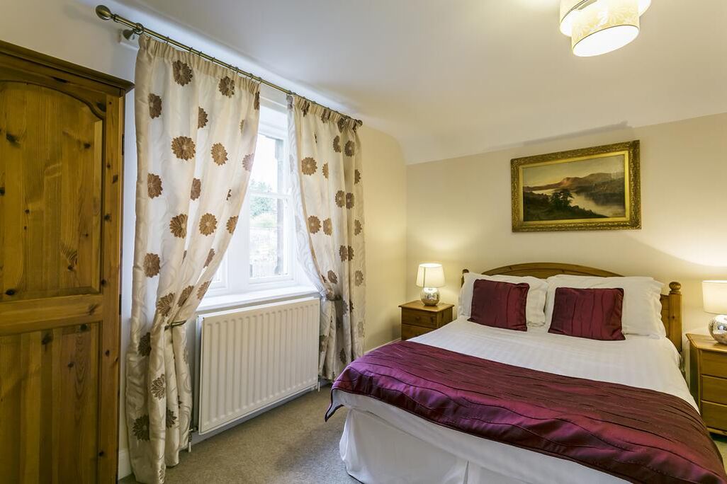 Une chambre à coucher avec un lit, des rideaux, un tableau, un radiateur et une armoire en bois.