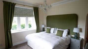 A neatly arranged bedroom with a large bed, green curtains, a chandelier, and two bedside tables with lamps.