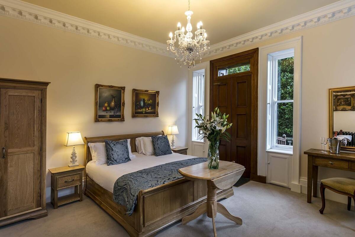 A bedroom with a wooden bed, two bedside tables with lamps, a chandelier, and two framed paintings on the wall.