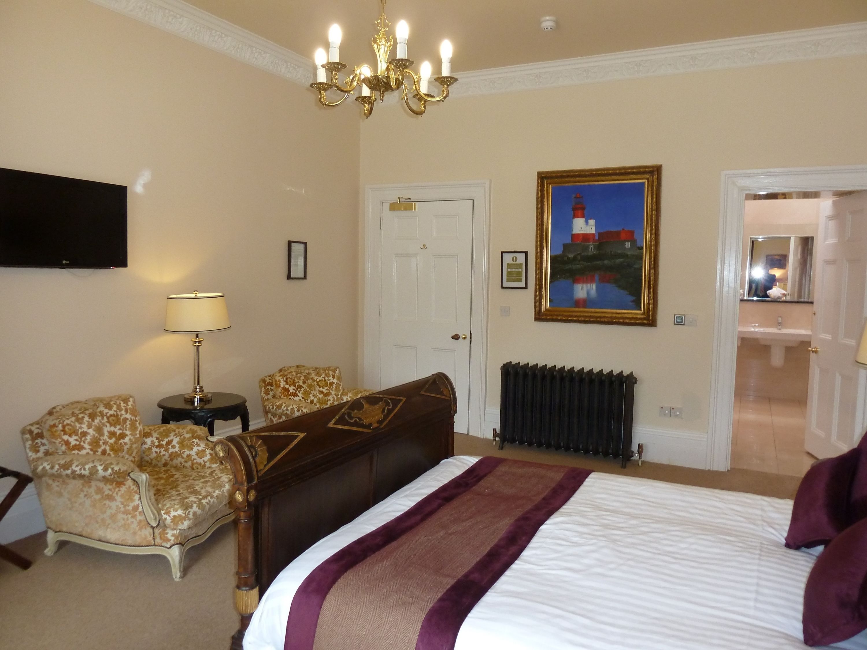 A hotel room with a large bed, a chandelier, a painting, and a view of the bathroom.