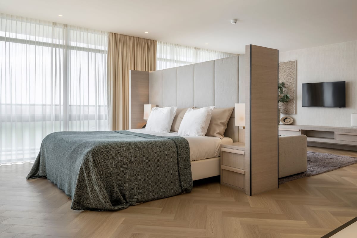 A modern hotel room with a large bed, a TV, and a wooden floor.