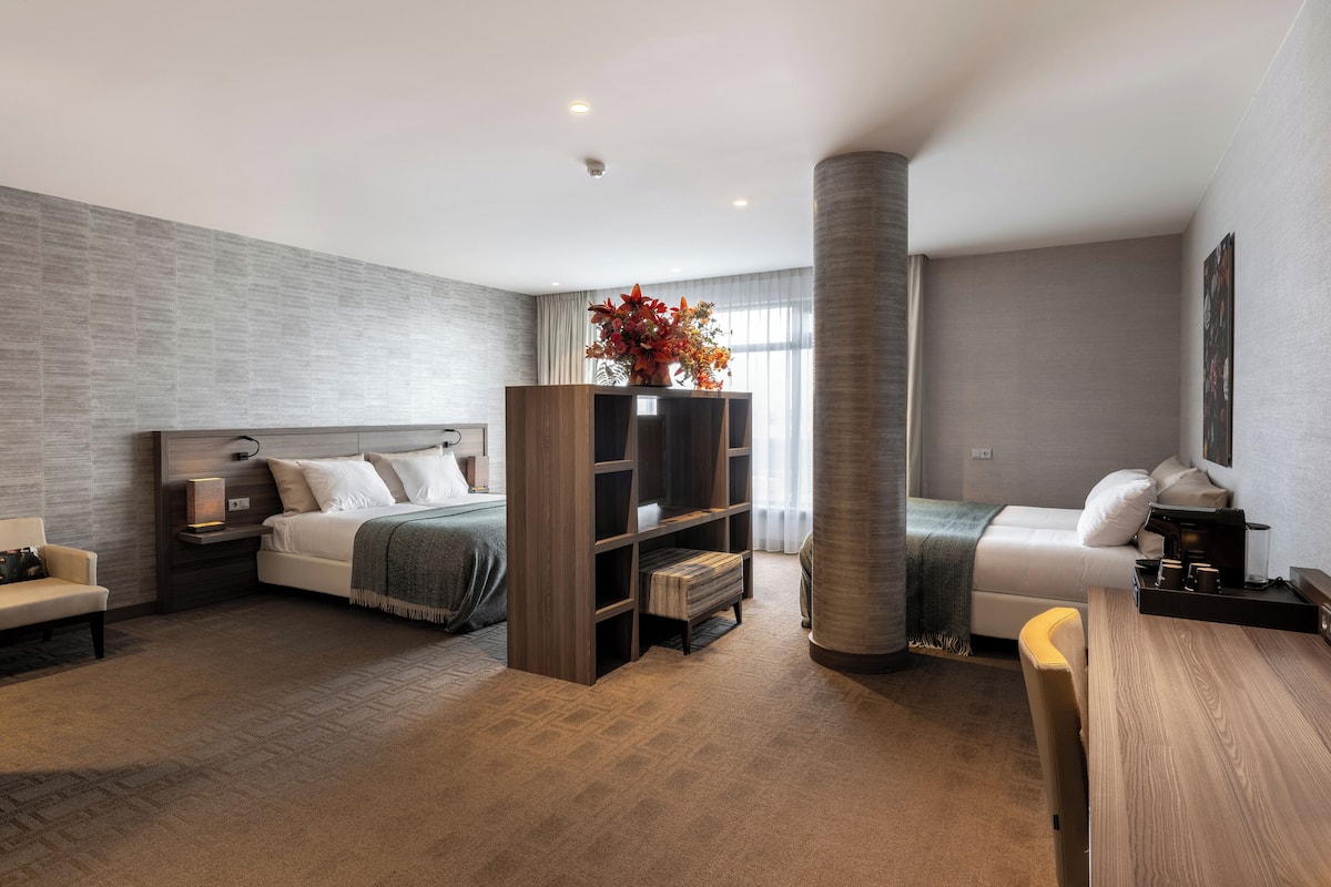 A modern hotel room with a bed, a sofa, a wooden bookshelf, and a coffee table.