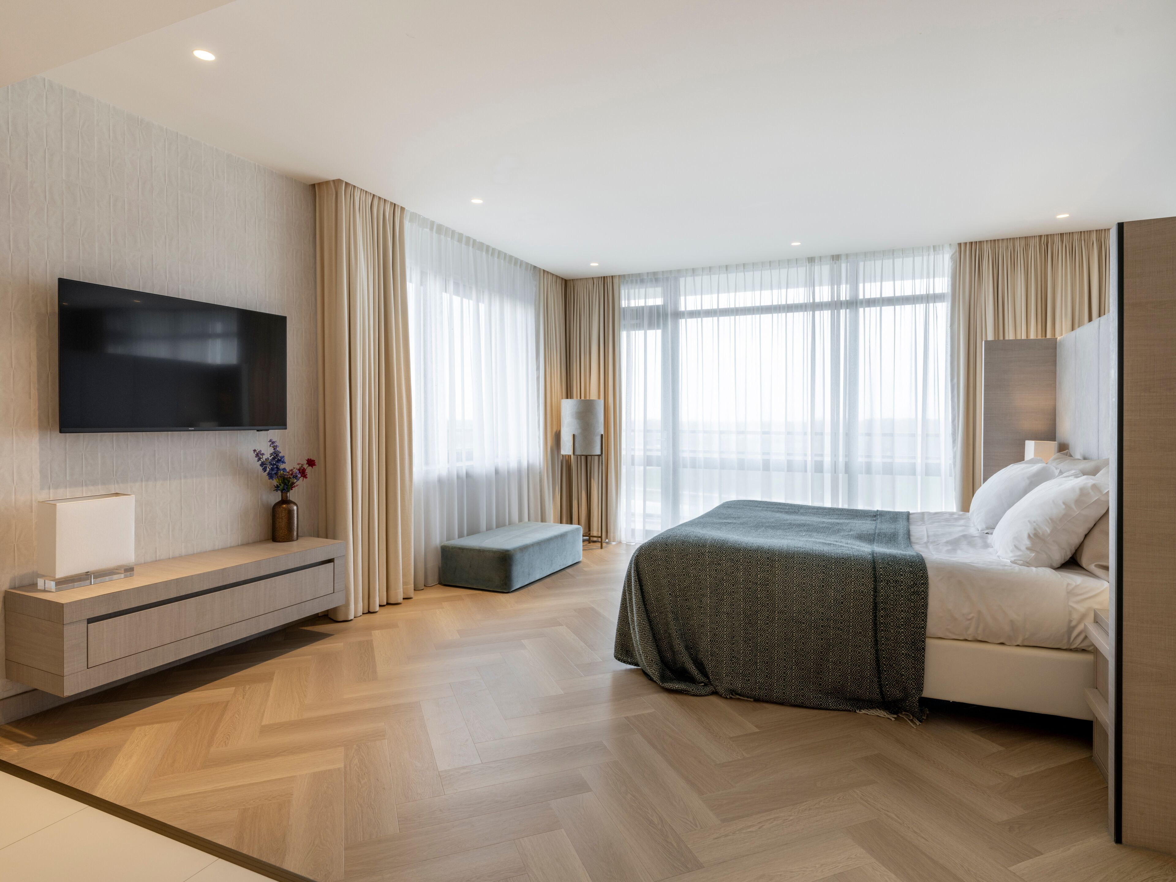 A modern hotel room with a large bed, a flat-screen TV, a bedside table, and a bench.