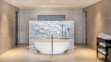 Une salle de bain moderne avec une baignoire sur pieds, une douche dotée d’un pommeau de douche à pluie et un porte-serviettes avec des serviettes pliées.